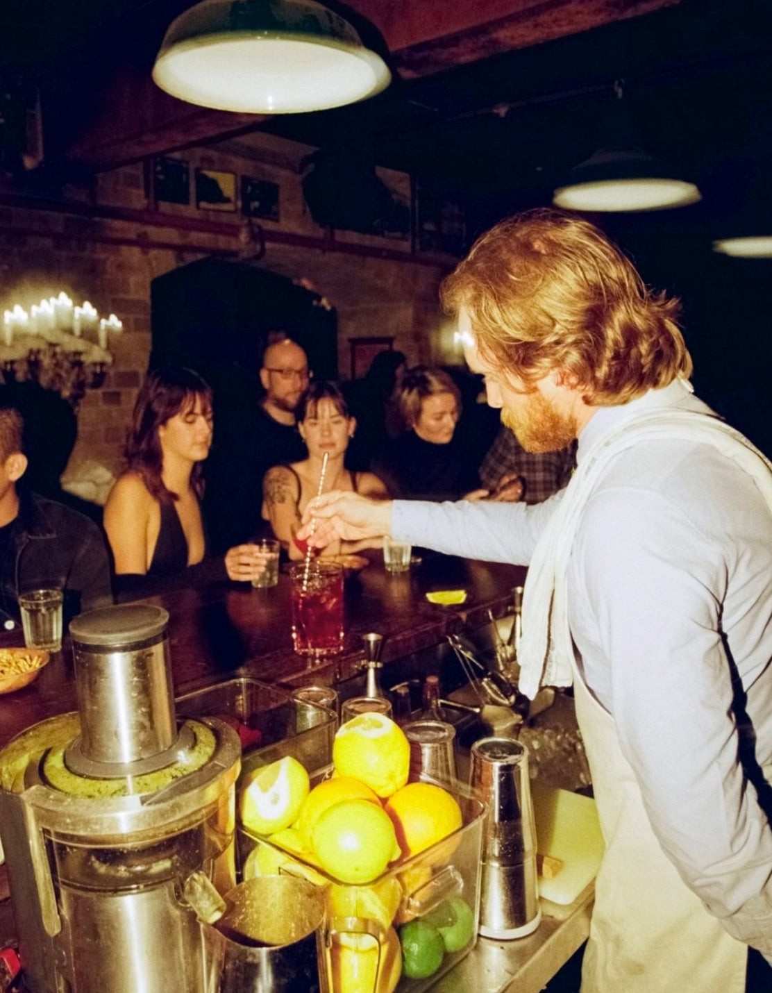 Bartenders at The Baxter Inn in Sydney, Australia, wearing dress shirts and white canvas aprons for a relaxed speakeasy vibe.