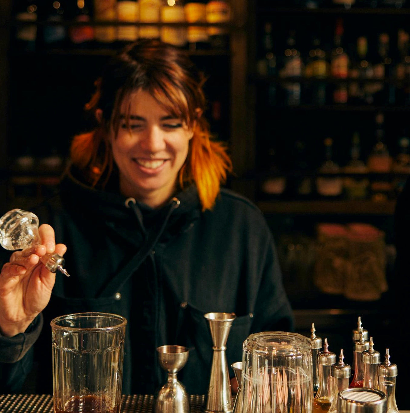 Bartender at Trick Dog San Francisco in a casual tee and grey denim apron, showcasing the bar's versatile and individualistic uniform policy.