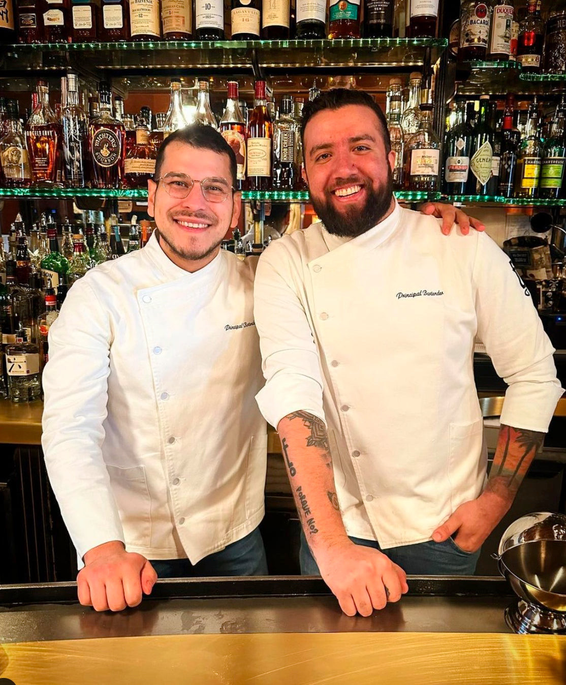 Bartender at Employees Only New York in a white jacket and denim waist apron, maintaining a classic Prohibition-era speakeasy bartender style.
