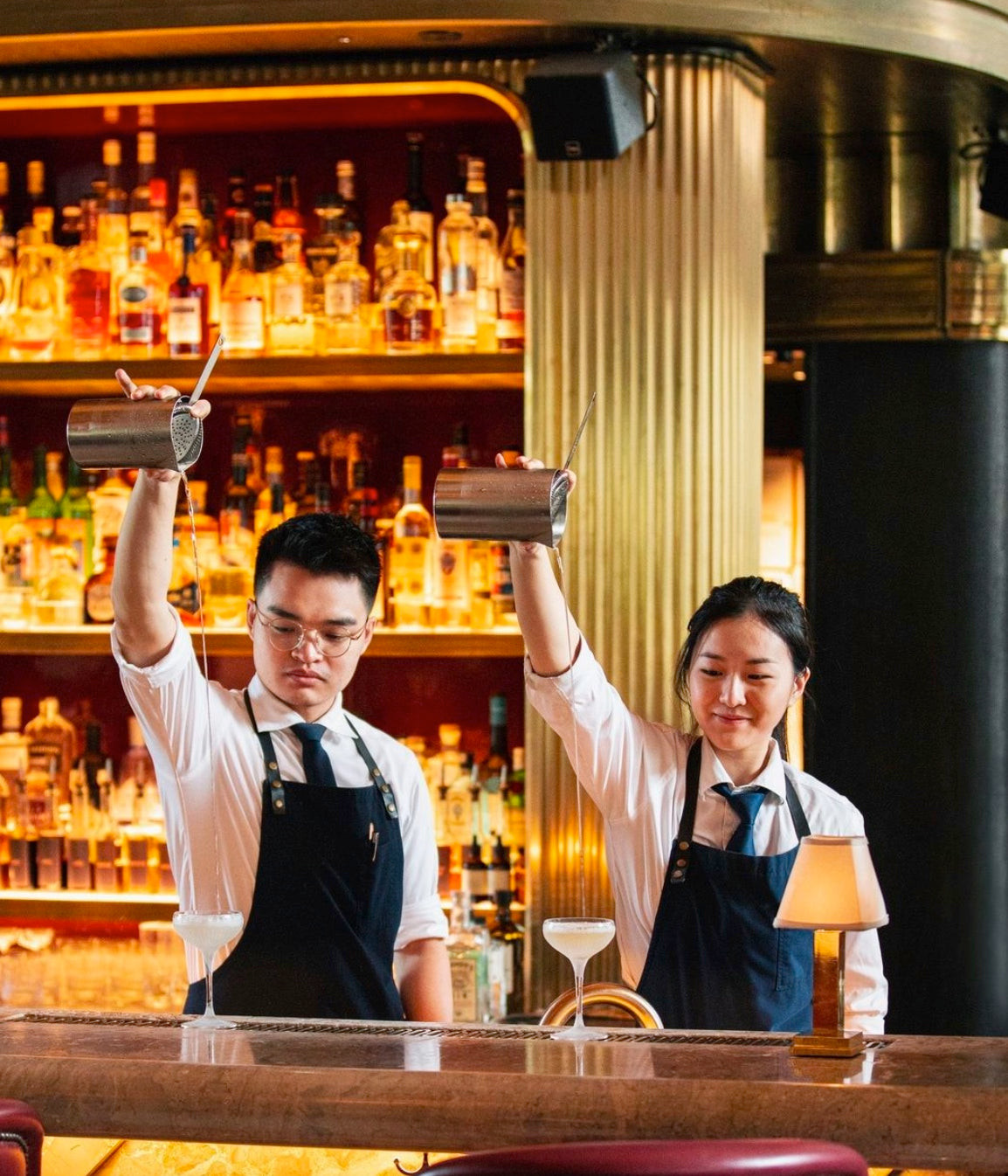 Bartender uniform detail at Atlas featuring a dark apron with gold stud buttons, adding a modern touch to classic elegance.