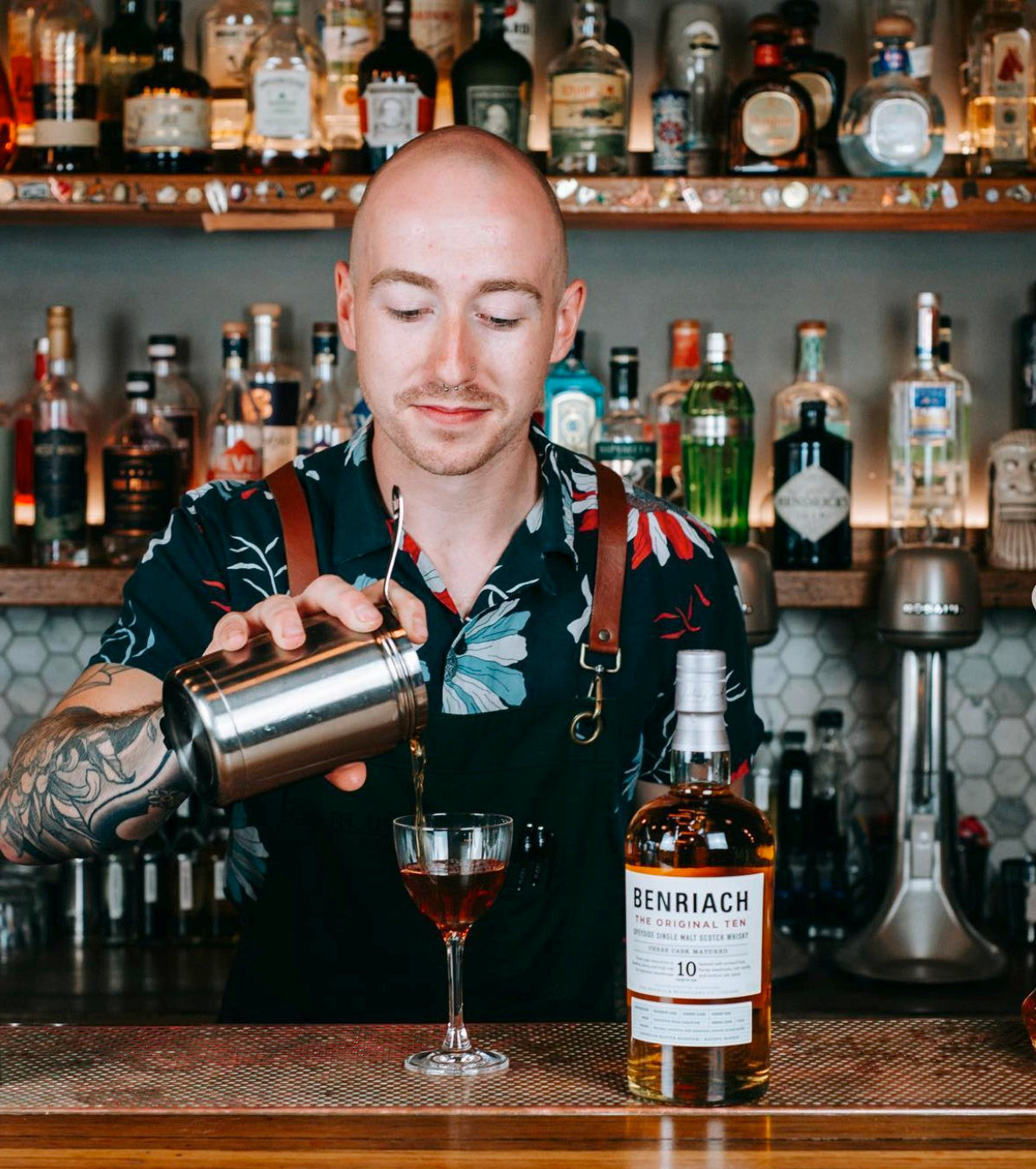Bartender at Black Pearl Fitzroy in a patterned shirt and apron with brown straps, representing modern and chic Australian bar style.