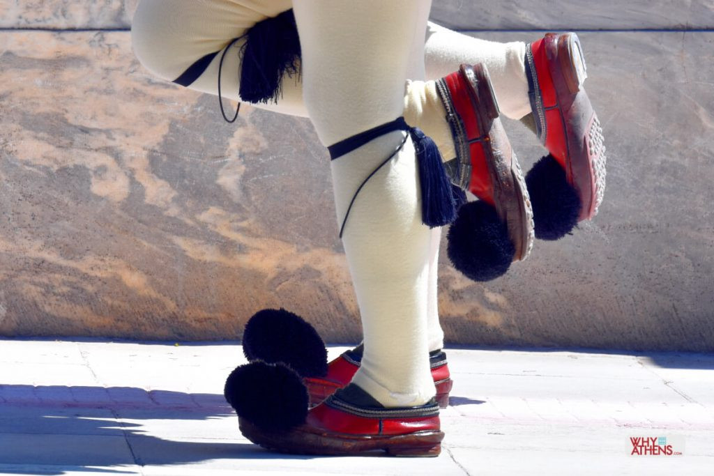Close-up of the Tsarouchia shoes, showing the upward-pointing toe and black silk pom-pom