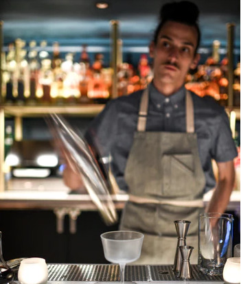 Bartender at Hotel Kansas City wearing a classic black suit with HKC logo pin, representing historical elegance with modern flair.