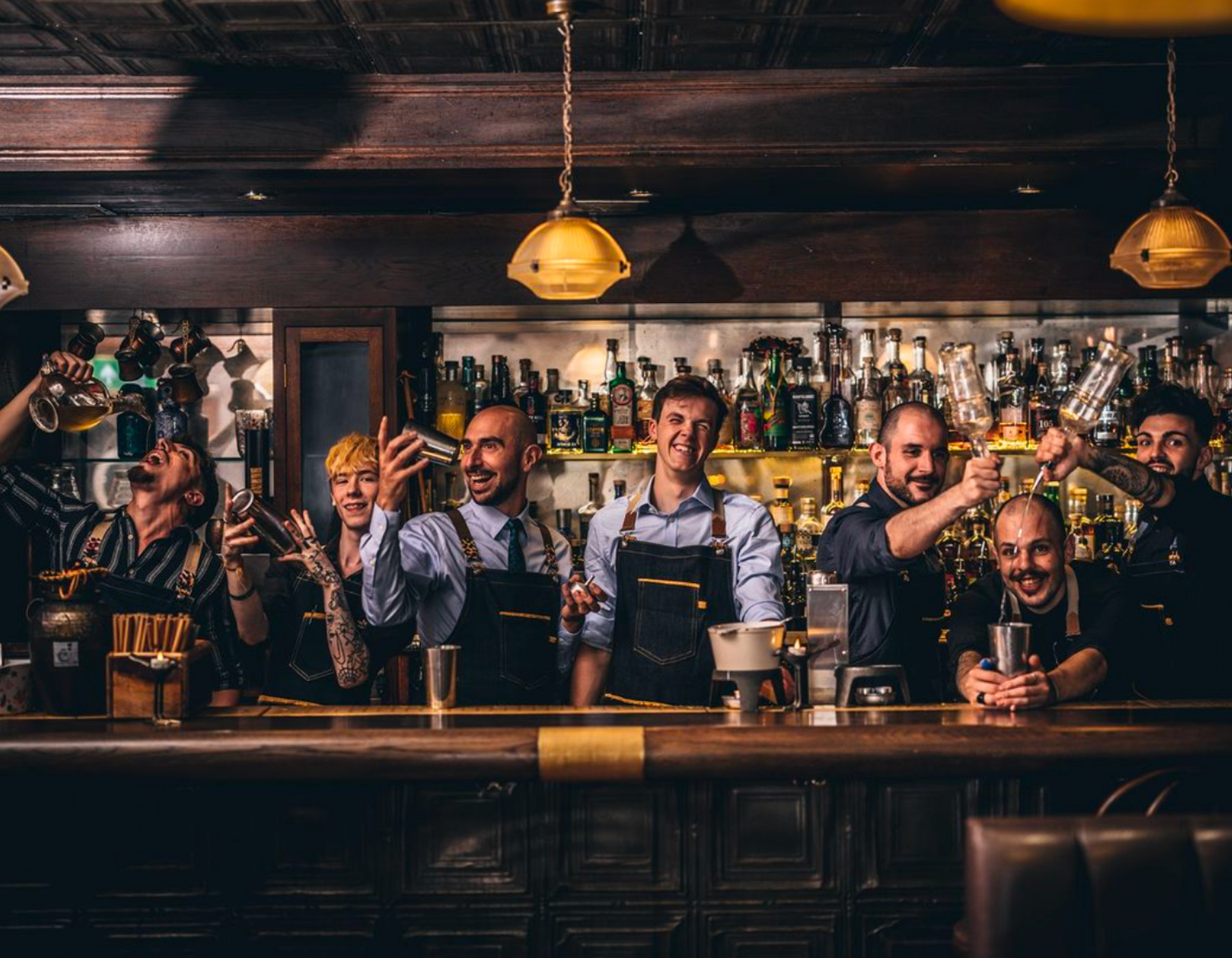 Bartender at Nightjar London wearing a floral apron over a dress shirt, highlighting the apron as a central uniform element in a speakeasy style.